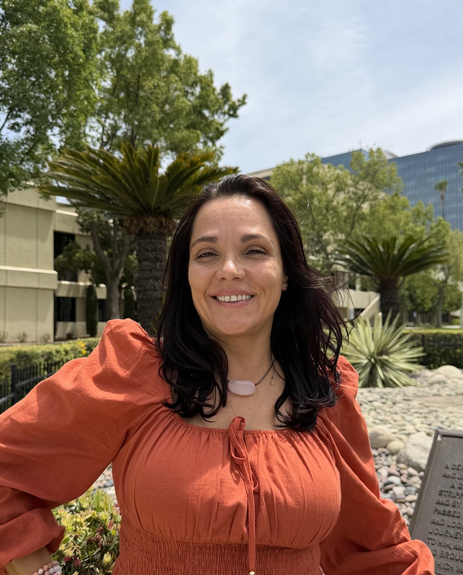 Adriana Lutti sorrindo ao ar livre, de blusa laranja, num jardim
